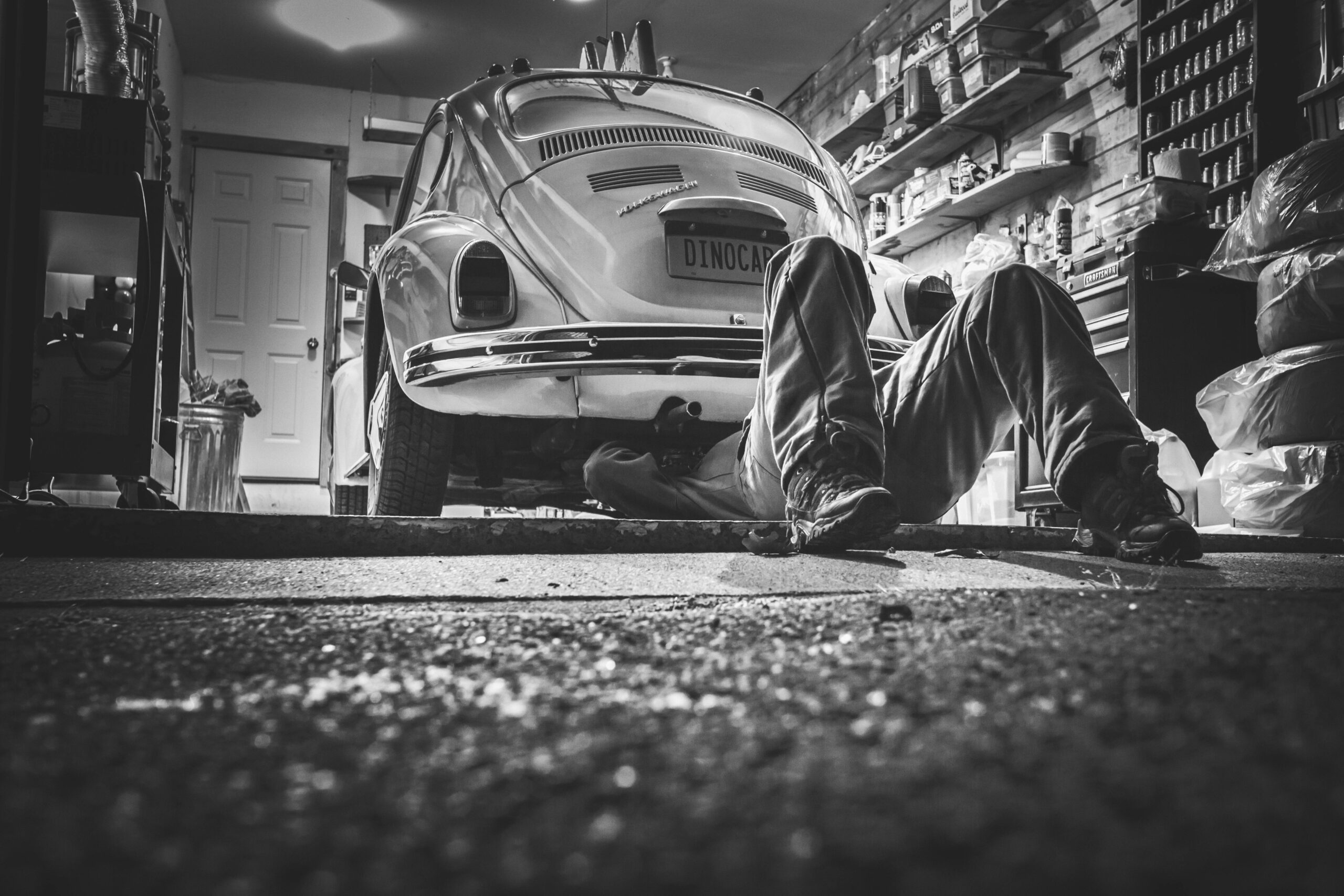Mechanic working beneath a classic Volkswagen Beetle in a vintage garage setting.