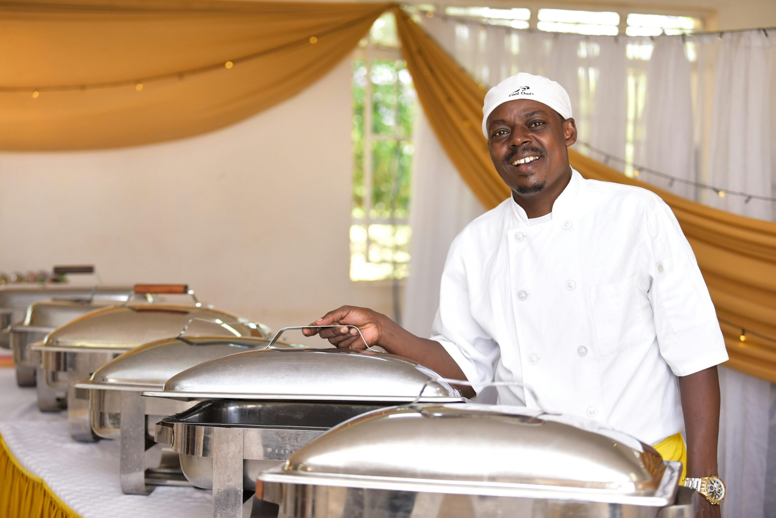 A cheerful chef stands by chafing dishes in a Nairobi hotel buffet setting.