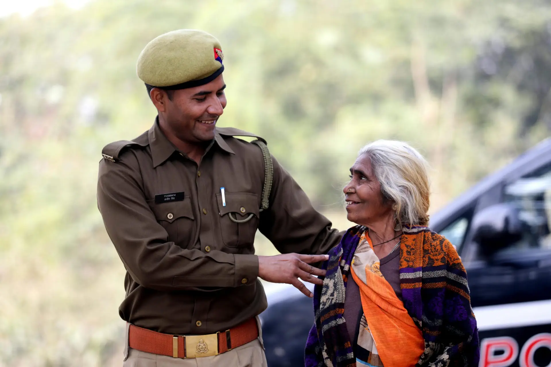 A smiling Indian police officer assists an elderly woman outdoors, showcasing community care.