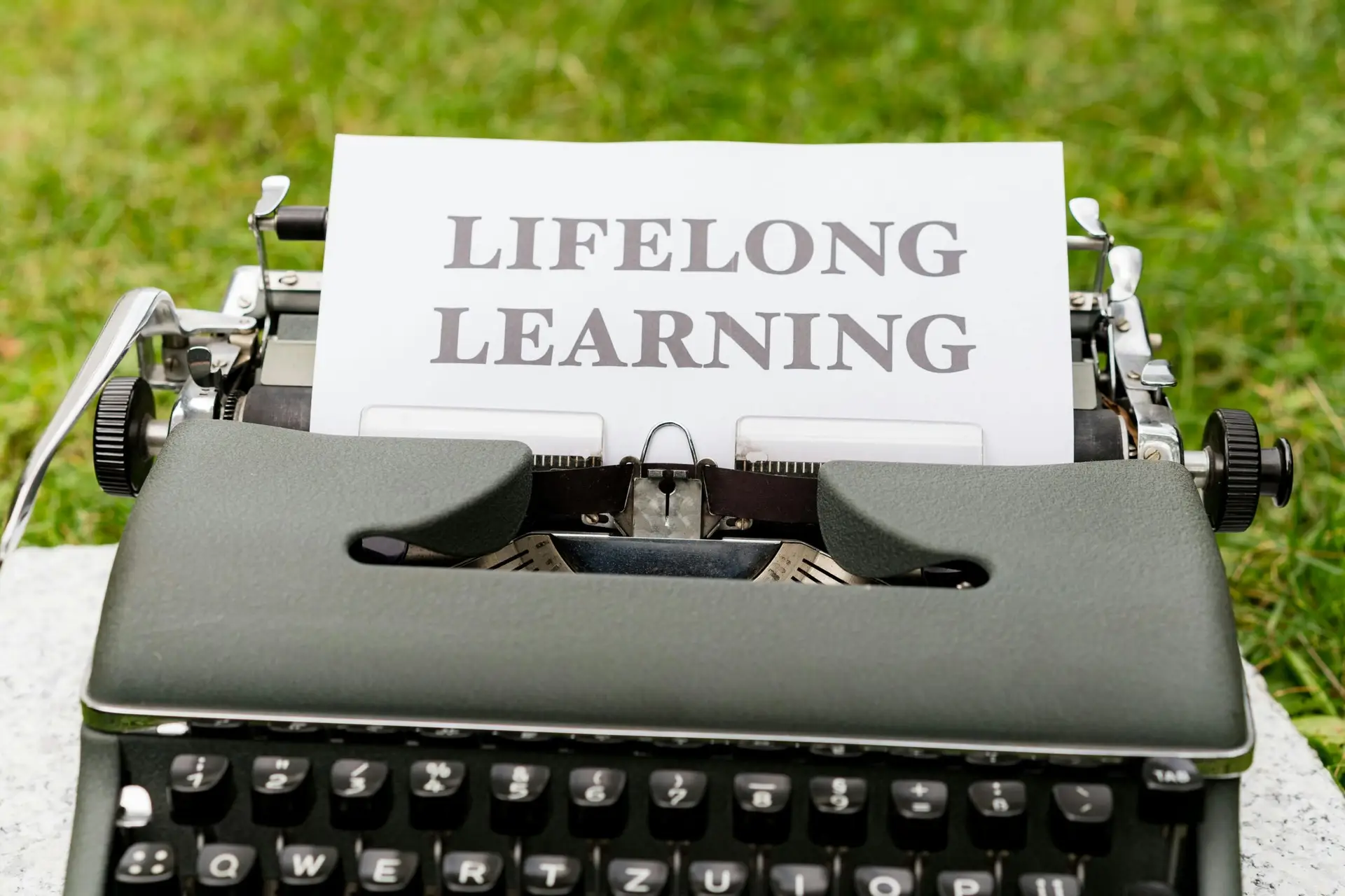 Close-up of a typewriter typing 'Lifelong Learning' outdoors, symbolizing continuous knowledge growth.