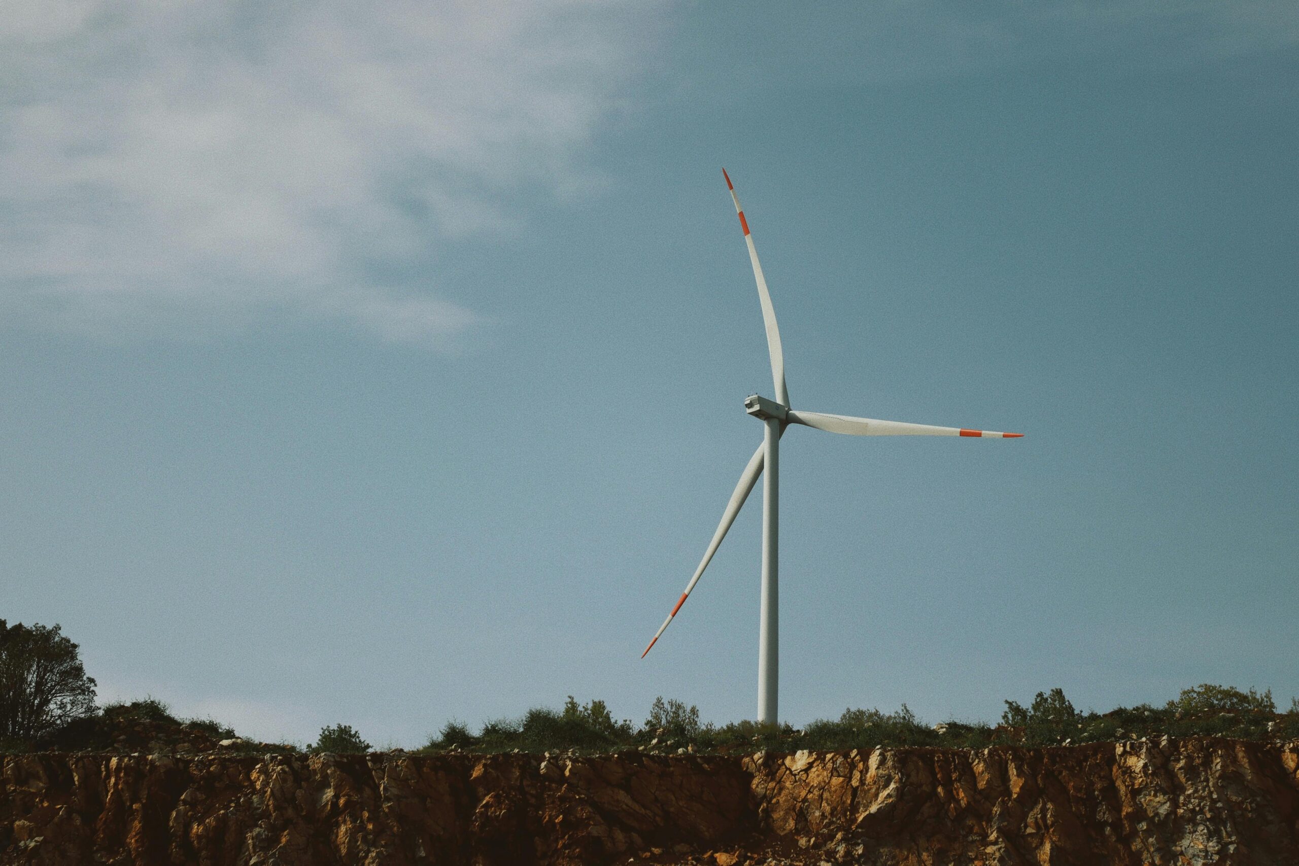 Single wind turbine on a rugged cliff with a clear blue sky, symbolizing renewable energy.