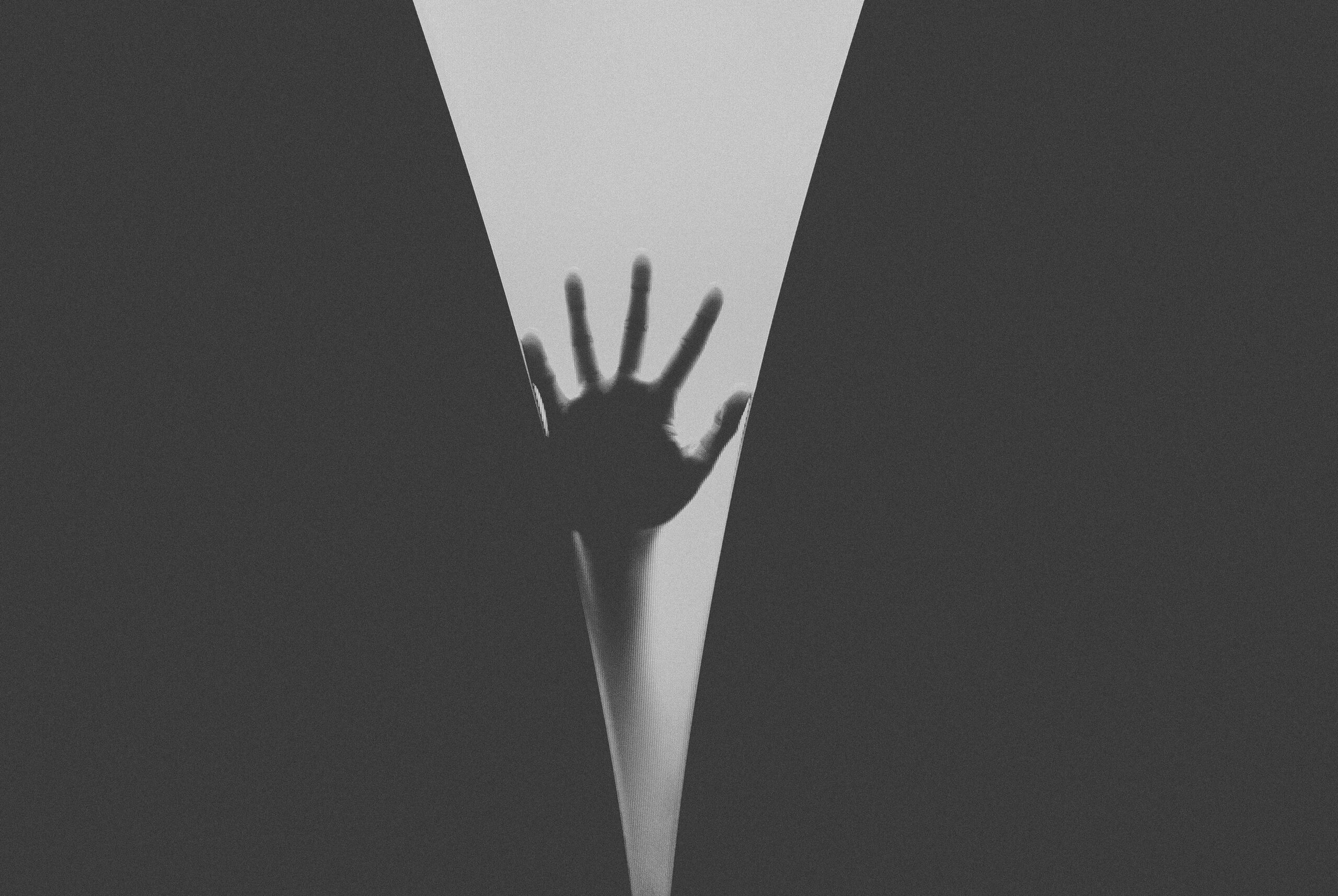 Artistic black and white silhouette of a hand pressing against frosted glass, creating a mysterious effect.