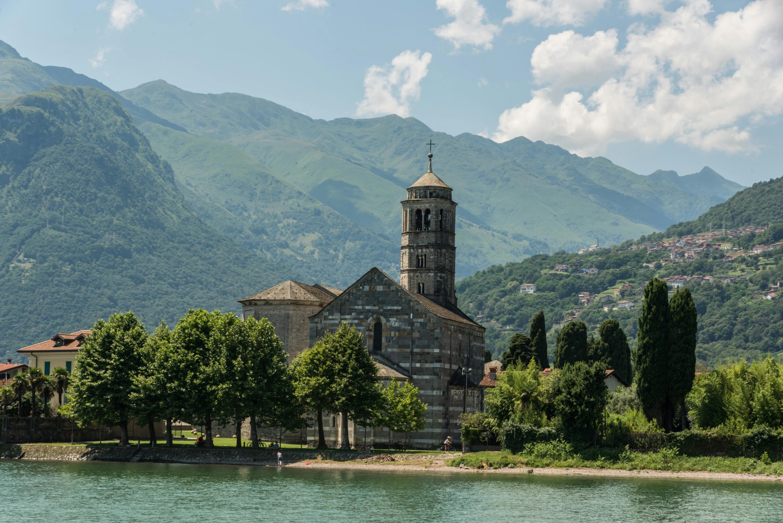 A picturesque view of a historic church surrounded by mountains in Lombardy, Italy.
