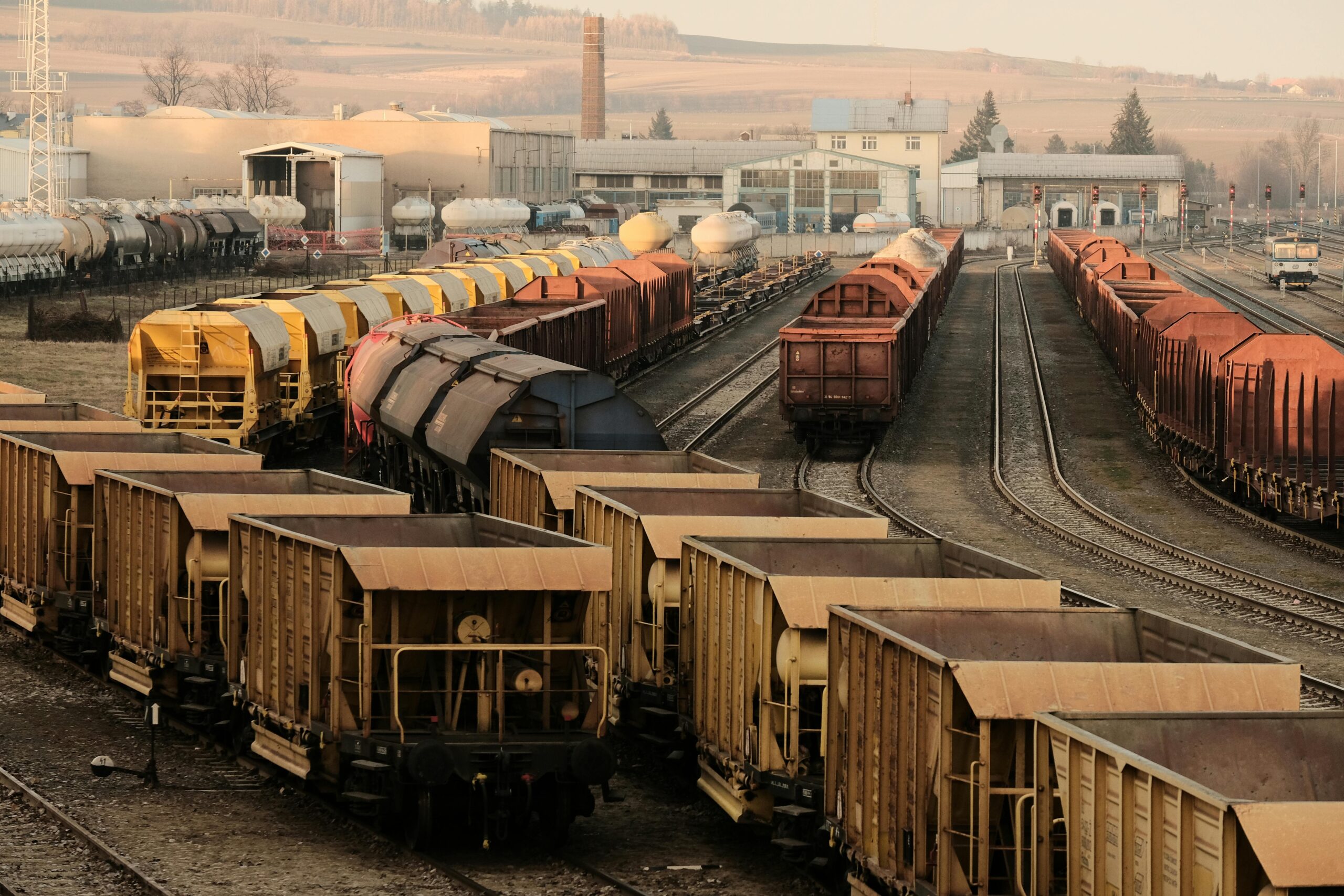 A busy freight train yard with multiple tracks and a variety of train cars in a rural setting.