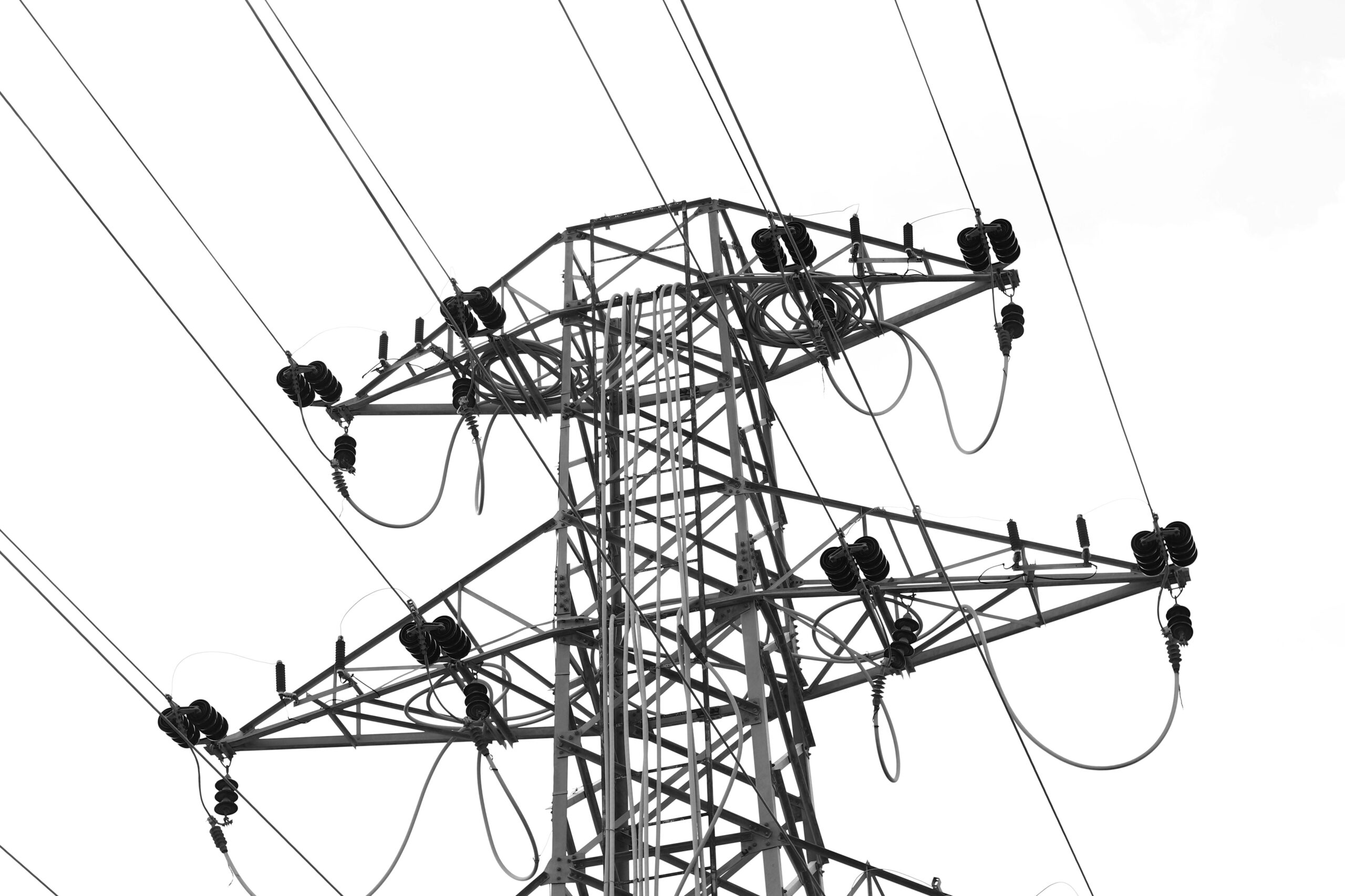 Black and white photo of high voltage power lines and electrical tower against a clear sky.