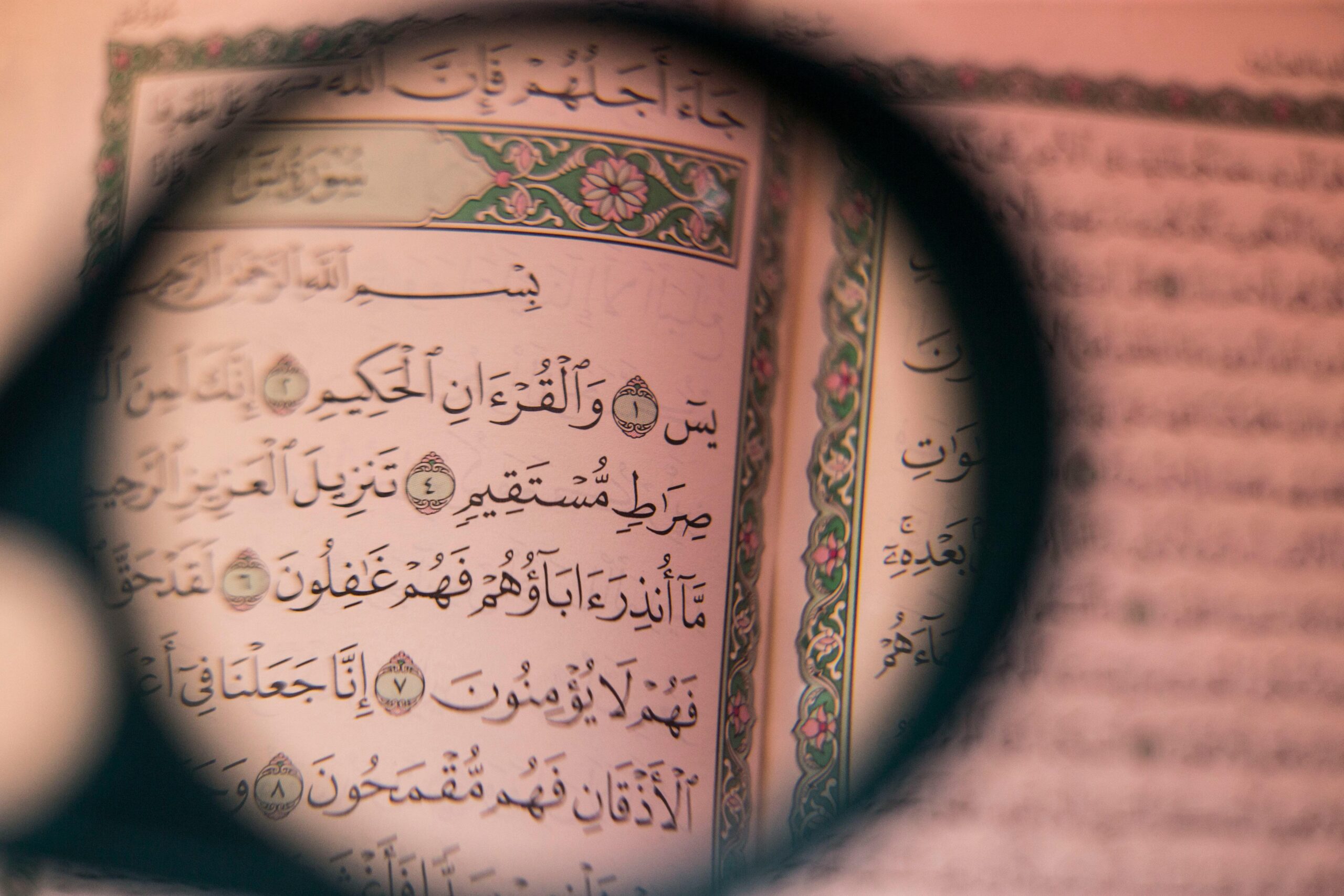 Close-up of Arabic script in the Quran viewed through a magnifying glass, symbolizing faith and study.