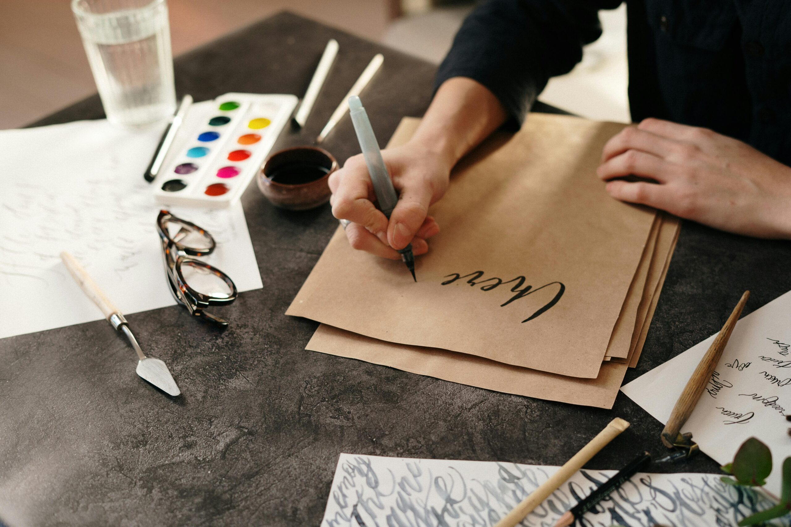 A person practicing calligraphy with ink, surrounded by art supplies on a table.