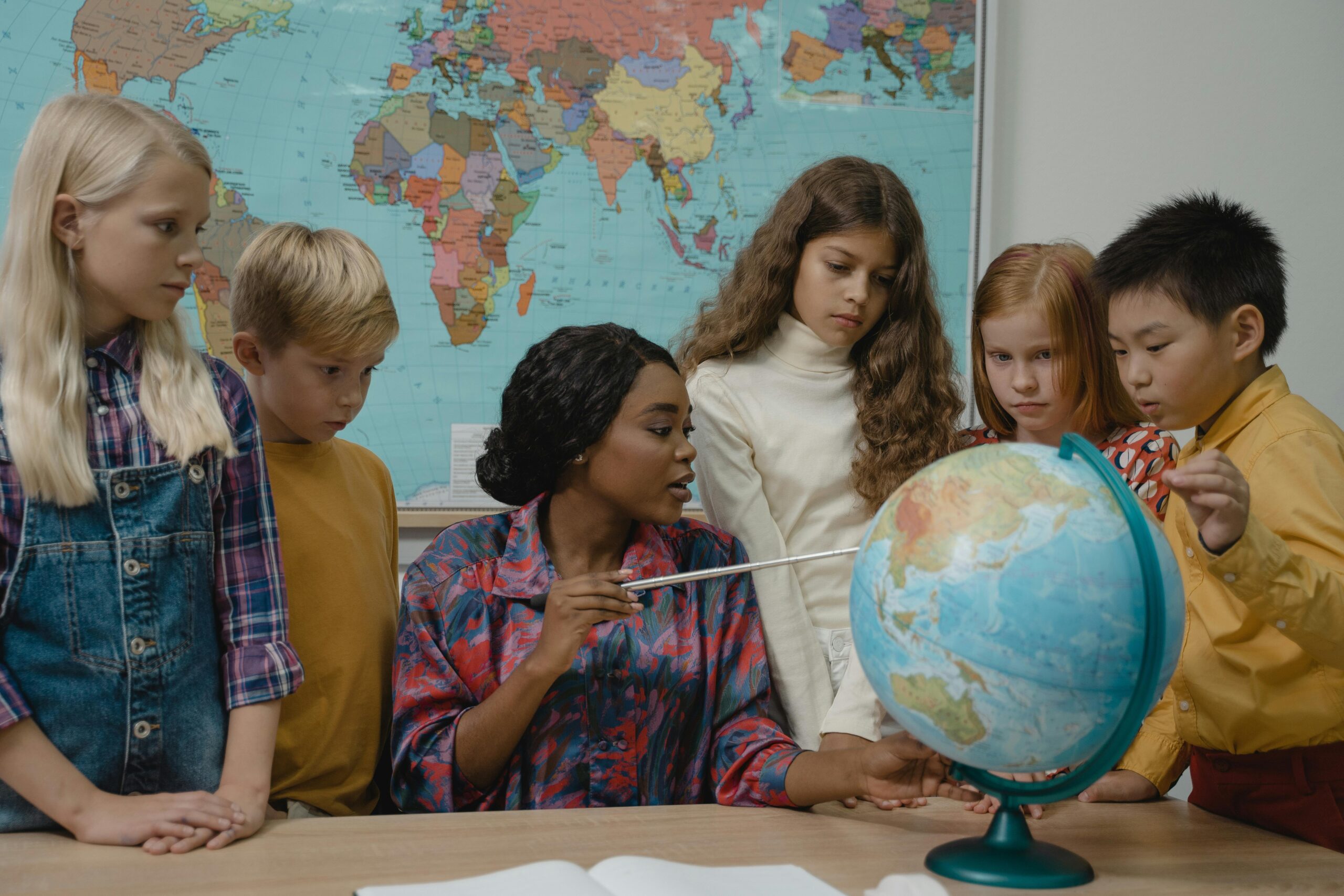 Diverse elementary students learning geography with a teacher and globe in the classroom.