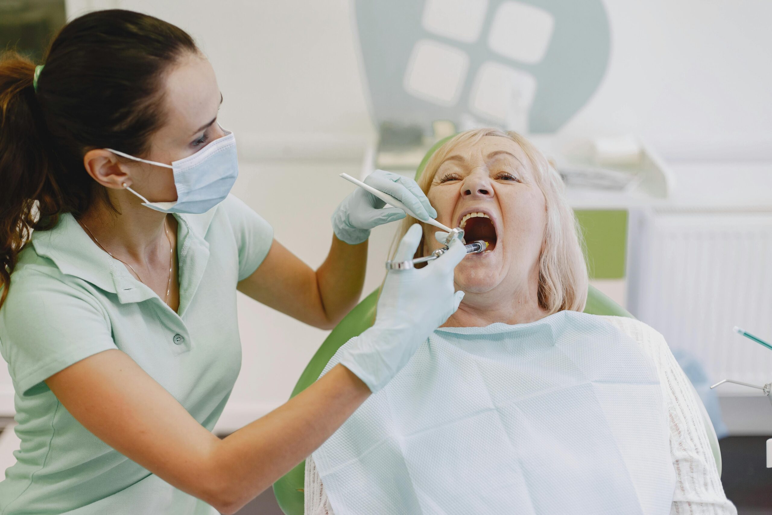 A female dentist examines a senior woman patient in a dental clinic setting.
