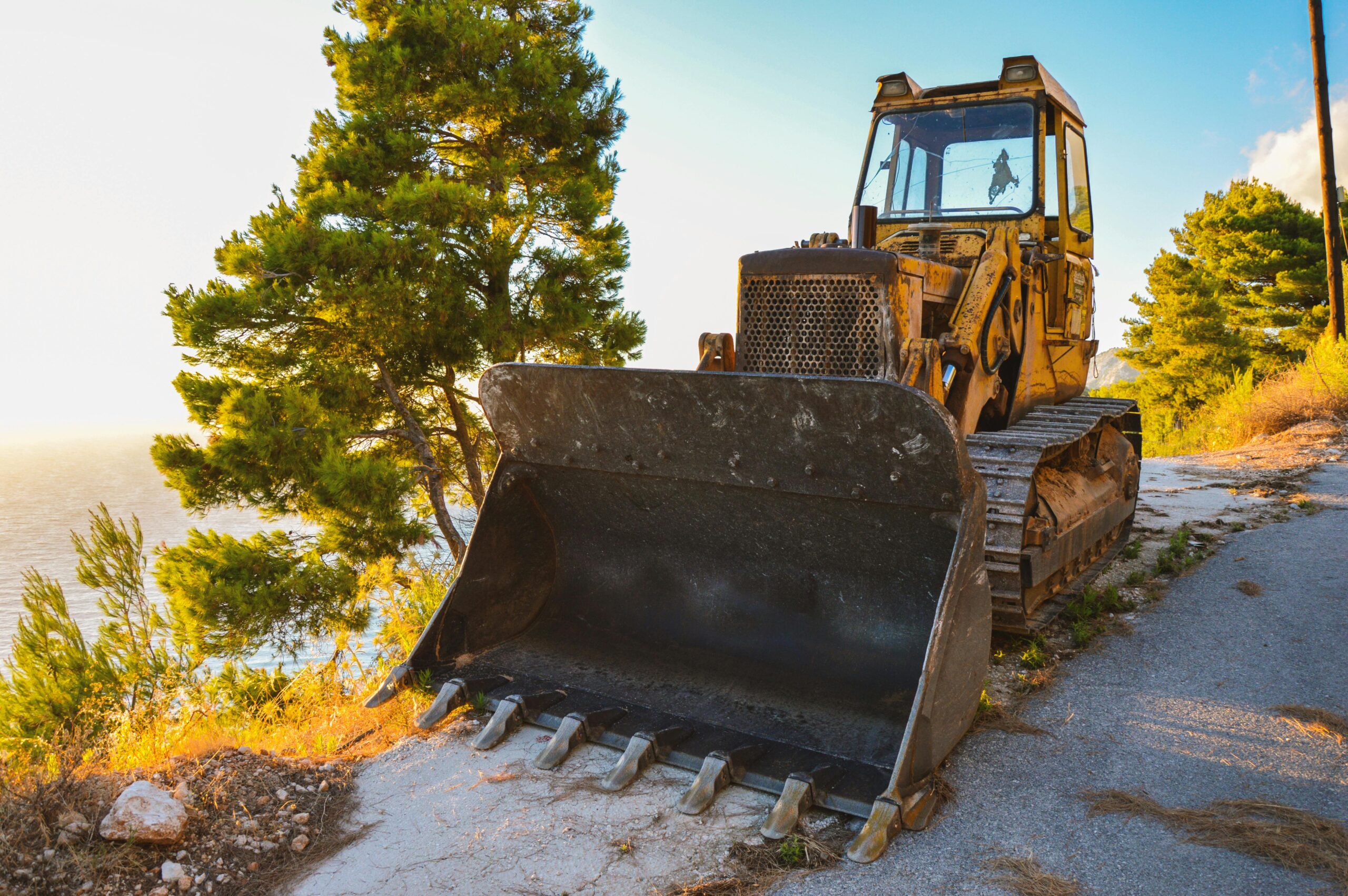 Sturdy bulldozer resting on a scenic roadside by the sea, bathed in warm summer sunlight.