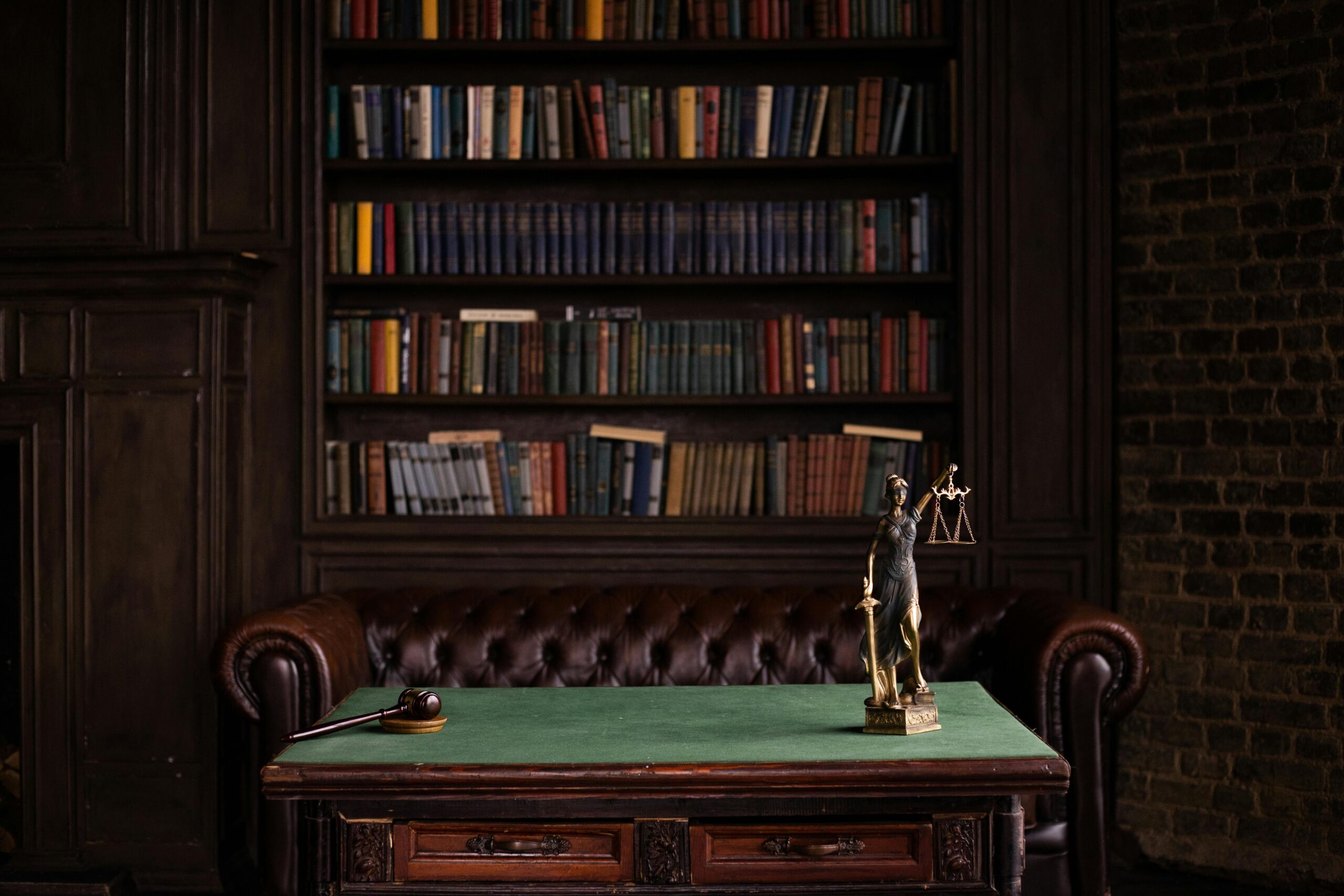 A classic study room with shelves of books, a gavel, and Lady Justice figurine on a green table.