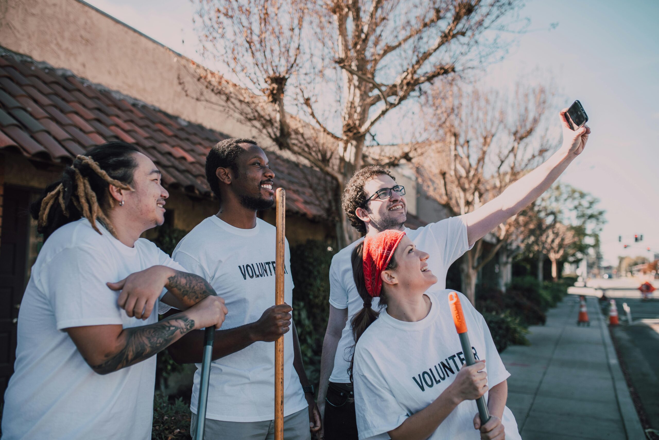 A diverse group of volunteers wearing white shirts and taking a selfie outdoors.