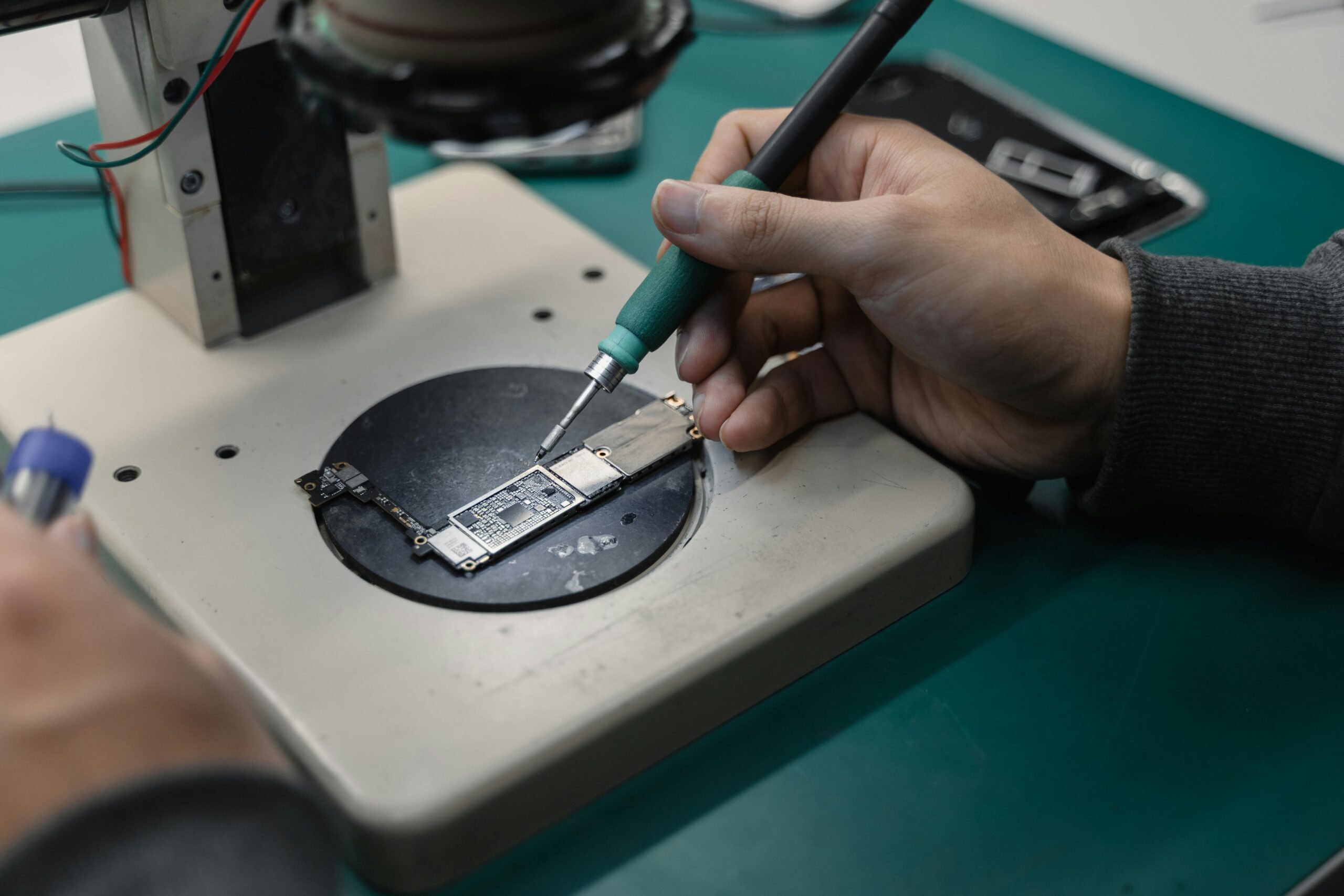 Detail view of hands soldering a circuit board in an electronics workshop.