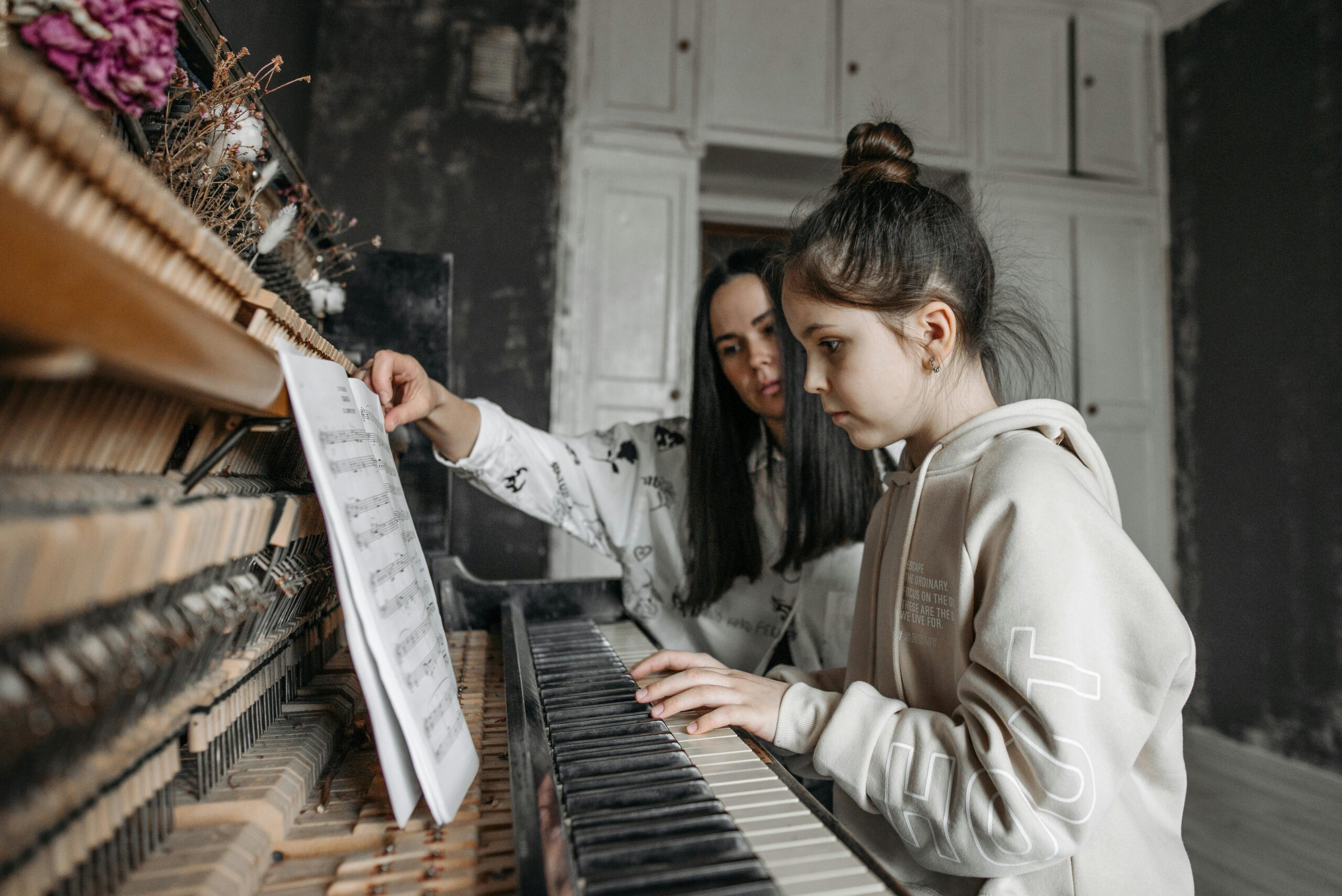 Young girl learning piano with her teacher in a music studio, focusing on sheet music.