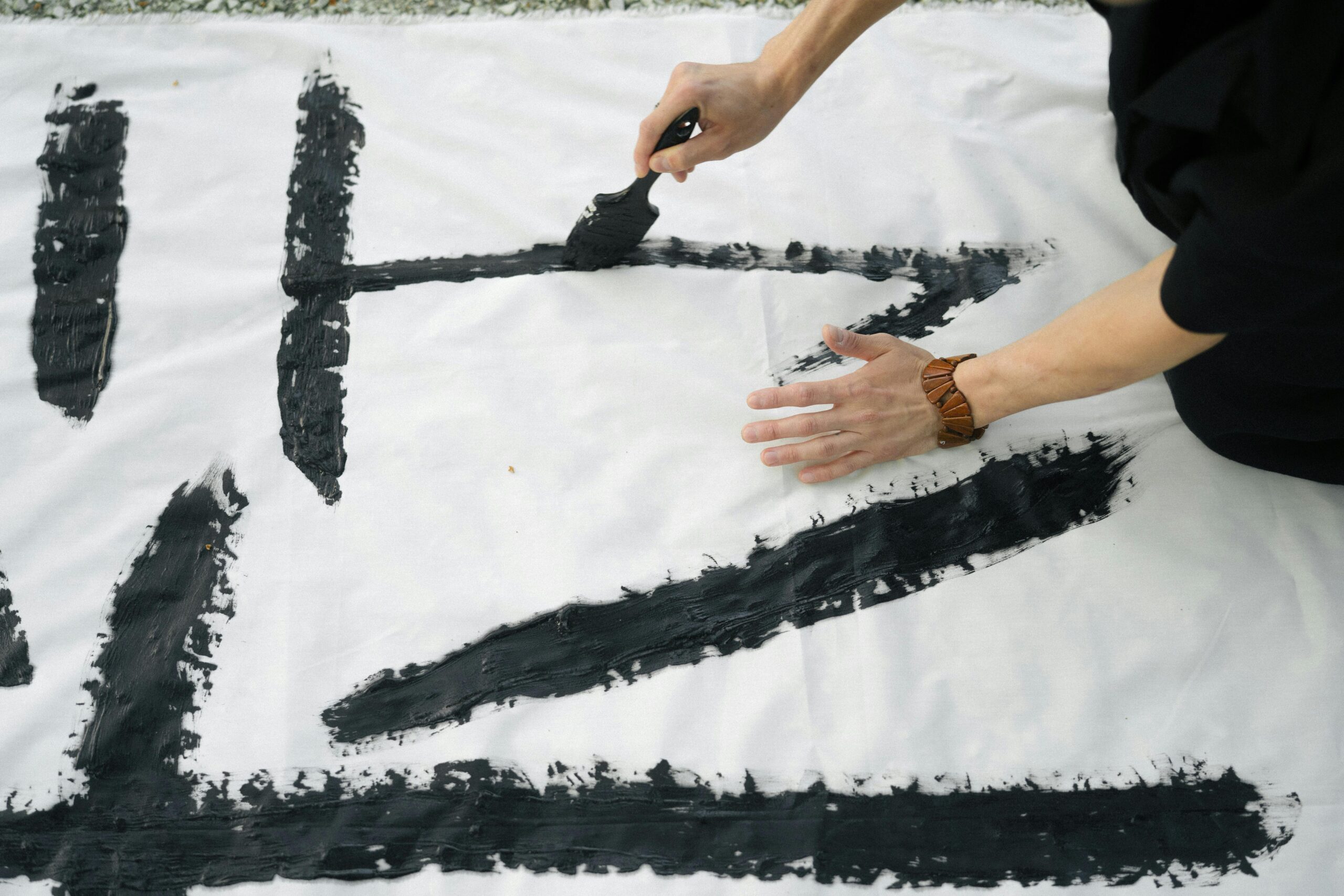 Close-up of artistic Japanese calligraphy being created on a white canvas outdoors.