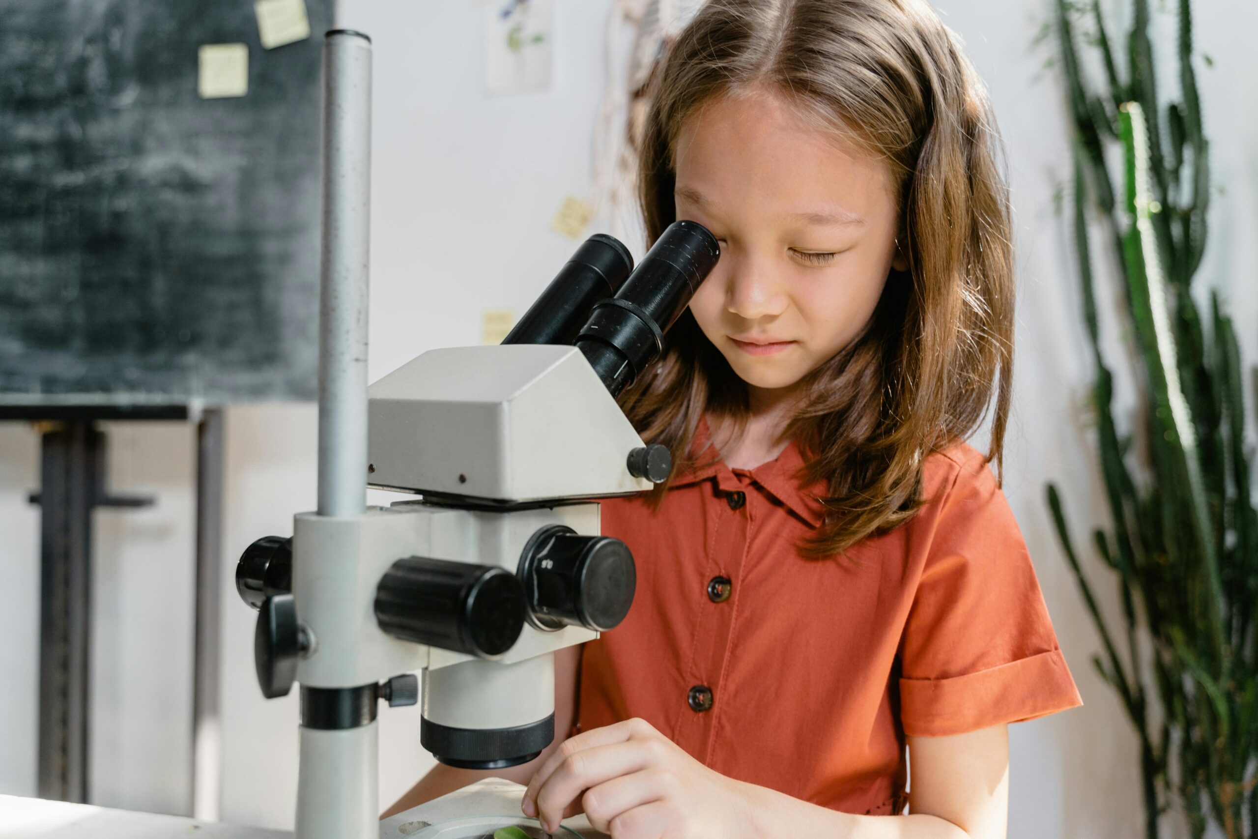 A curious girl examining a sample using a microscope in a classroom setting, focused on learning science.