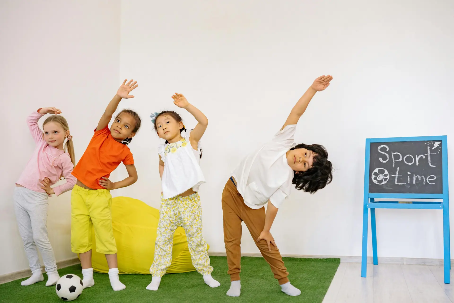 Joyful children stretching during indoor sport time in a classroom.