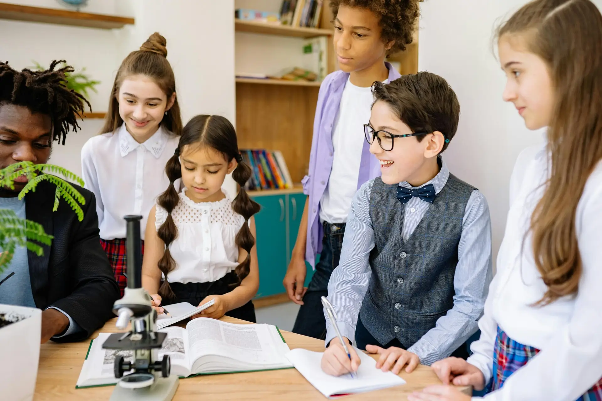 Group of children learning with microscope in a classroom setting, exploring science.