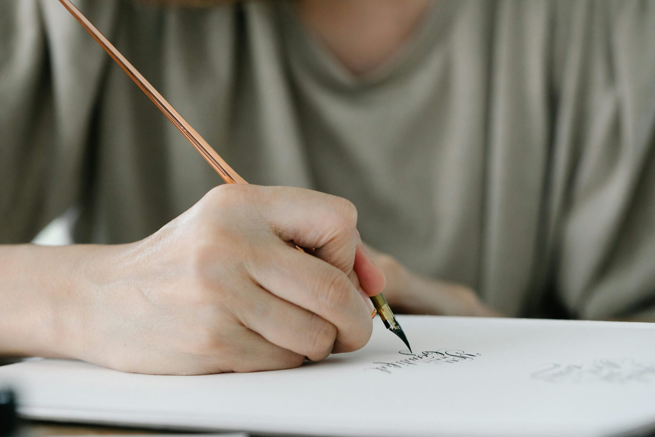 A close-up shot of a person using a calligraphy pen to write elegantly on paper.