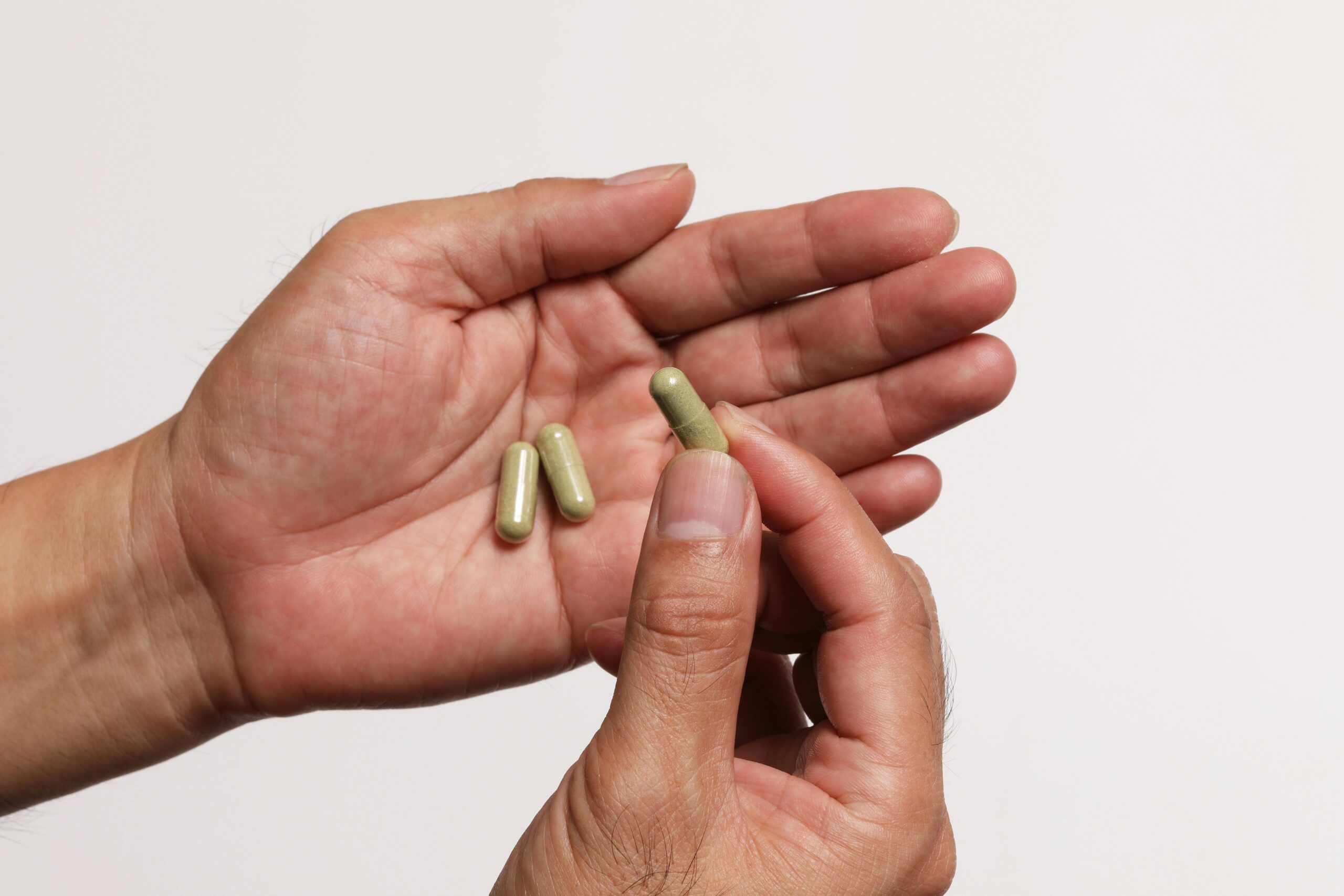 Male hands holding green capsules against a plain white background, emphasizing supplement intake.